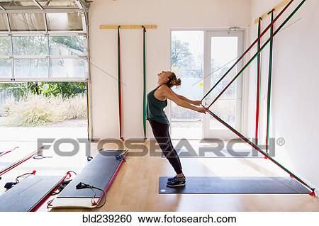 Stock Image - Caucasian woman using resistance bands in gymnasium. Fotosearch