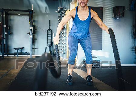 Stock Image - Caucasian woman using ropes in gymnasium. Fotosearch
