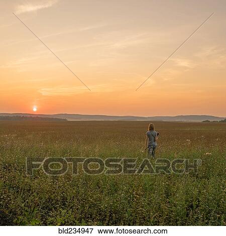 Stock Photo - Caucasian woman walking in field at sunset. Fotosearch