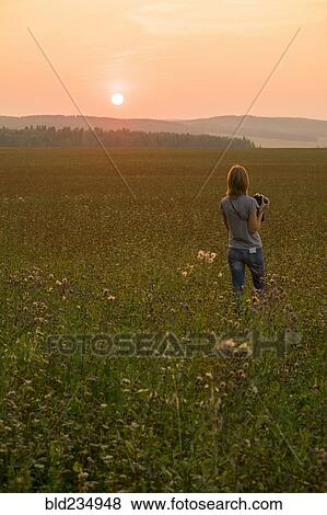 Caucasian woman walking in field at sunset with camera View Large Photo Image Stock Photo - Caucasian woman walking in field at sunset with camera. Fotosearch