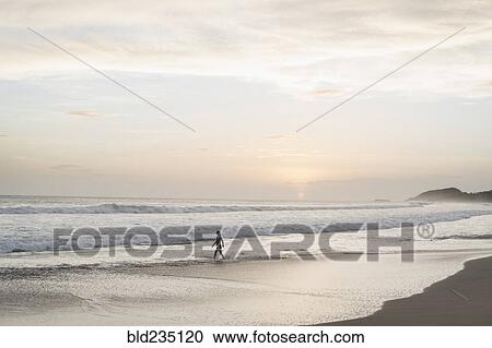 Stock Image - Caucasian woman walking on beach at sunset. Fotosearch