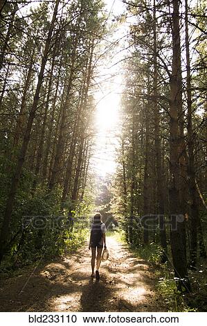 Stock Image - Caucasian woman walking on tree-lined forest path. Fotosearch
