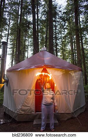 Stock Photo - Caucasian woman waving sparkler outside yurt. Fotosearch