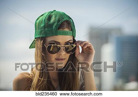 Caucasian woman wearing baseball cap peering over sunglasses View Large Photo Image Stock Image - Caucasian woman wearing baseball cap peering over sunglasses. Fotosearch