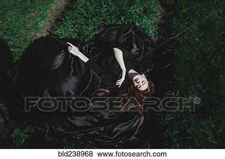 Stock Photo - Caucasian woman wearing black dress sleeping on grass. Fotosearch