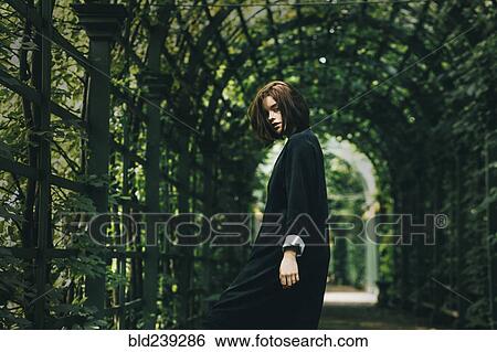 Stock Photograph - Caucasian woman wearing black dress under foliage. Fotosearch
