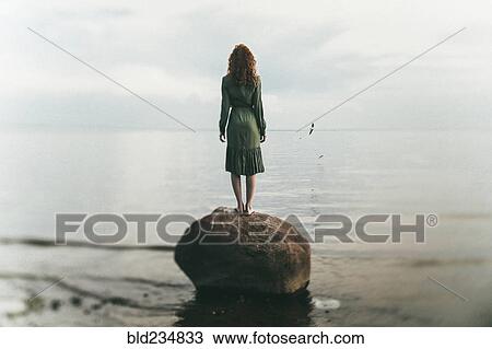 Caucasian woman wearing dress standing on rock at beach View Large Photo Image Stock Image - Caucasian woman wearing dress standing on rock at beach. Fotosearch