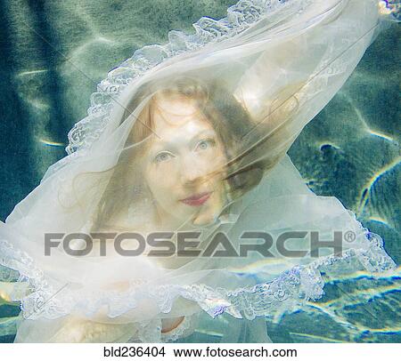Picture - Caucasian woman wearing dress swimming underwater. Fotosearch