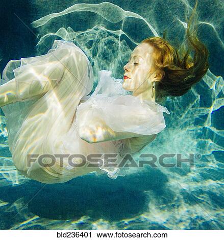 Stock Image - Caucasian woman wearing dress swimming underwater. Fotosearch