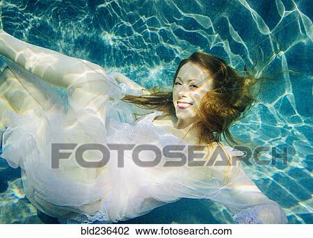 Stock Image - Caucasian woman wearing dress swimming underwater. Fotosearch