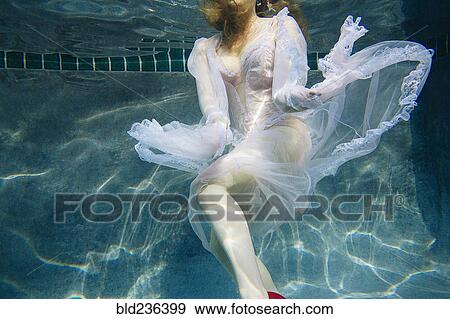 Stock Photo - Caucasian woman wearing dress swimming underwater. Fotosearch