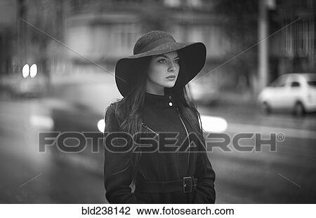 Stock Image - Caucasian woman wearing hat and coat in city. Fotosearch