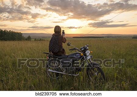 Caucasian woman with motorcycle in field photographing sunset View Large Photo Image Stock Photography - Caucasian woman with motorcycle in field photographing sunset. Fotosearch