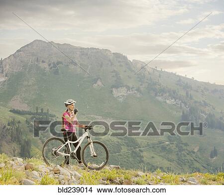 Picture - Caucasian woman with mountain bike drinking from backpack. Fotosearch