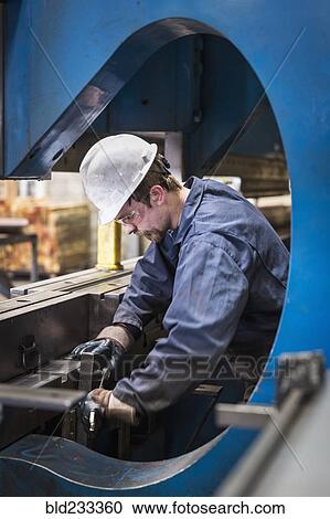 Stock Image - Caucasian worker fabricating metal in factory. Fotosearch