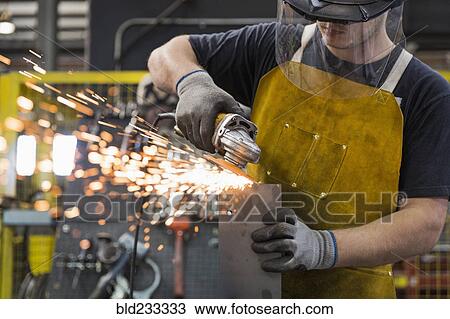 Stock Image - Caucasian worker grinding metal in factory. Fotosearch