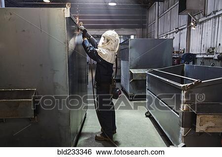 Stock Photograph - Caucasian worker grinding metal container in factory. Fotosearch