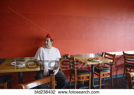 Stock Image - Chef sitting at table in pizzeria. Fotosearch