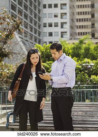 Stock Photograph - Chinese business people texting on cell phone near city bench. Fotosearch