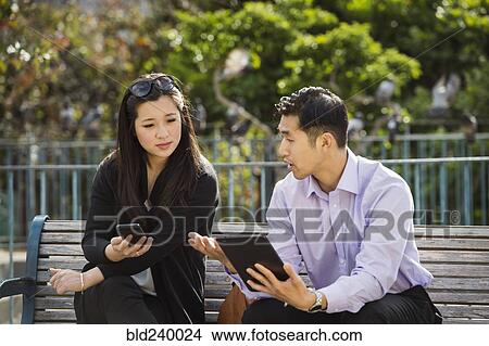Picture - Chinese business people using technology on city bench. Fotosearch