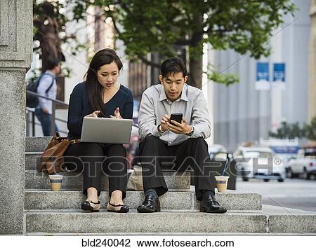 Stock Image - Chinese business people using technology during lunch in city. Fotosearch