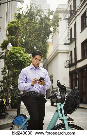 Stock Image - Chinese businessman on bicycle texting on cell phone. Fotosearch