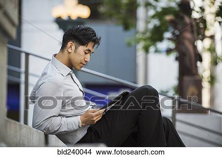 Chinese businessman reading digital tablet on staircase View Large Photo Image Picture - Chinese businessman reading digital tablet on staircase. Fotosearch