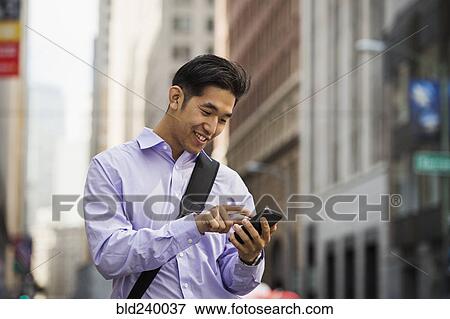 Stock Photo - Chinese businessman texting on cell phone in city. Fotosearch