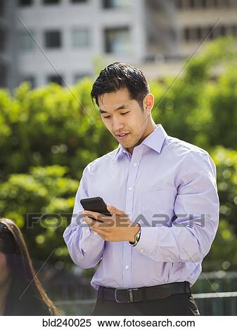 Stock Photography - Chinese businessman texting on cell phone outdoors. Fotosearch