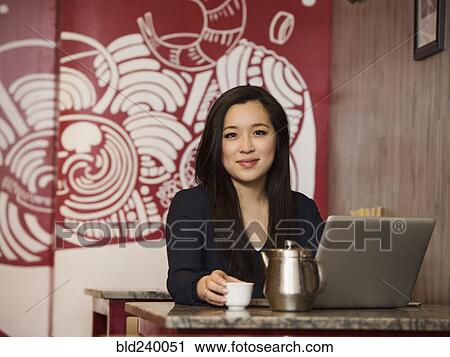 Stock Image - Chinese businesswoman drinking tea and using laptop. Fotosearch