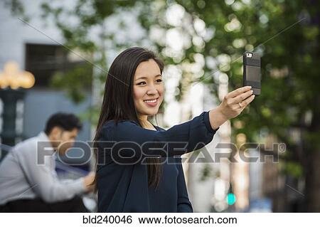 Chinese businesswoman posing for cell phone selfie outdoors View Large Photo Image Stock Photograph - Chinese businesswoman posing for cell phone selfie outdoors. Fotosearch