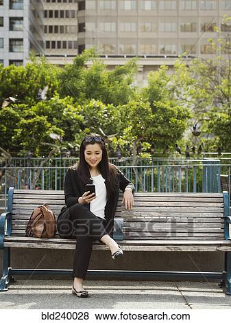 Stock Photo - Chinese businesswoman texting on cell phone on city bench. Fotosearch