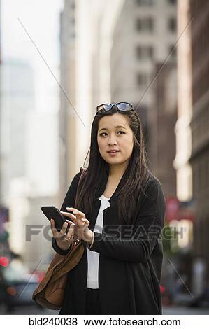 Stock Photo - Chinese businesswoman texting on cell phone in city. Fotosearch