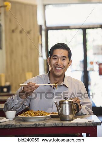 Stock Photo - Chinese man eating with chopsticks in restaurant. Fotosearch