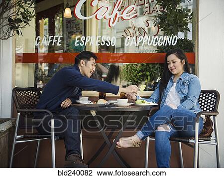 Stock Image - Chinese man tasting food of woman at outdoor cafe. Fotosearch