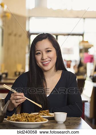 Stock Photo - Chinese woman eating with chopsticks in restaurant. Fotosearch