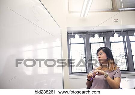 Stock Image - Chinese woman holding marker reading whiteboard. Fotosearch