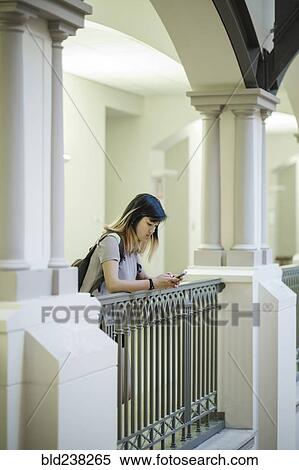 Stock Photography - Chinese woman leaning on railing texting on cell phone. Fotosearch