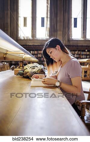 Picture - Chinese woman sitting in library reading book. Fotosearch