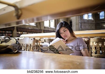 Stock Photograph - Chinese woman sitting in library reading book. Fotosearch