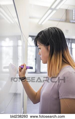 Stock Image - Chinese woman writing on whiteboard with marker. Fotosearch