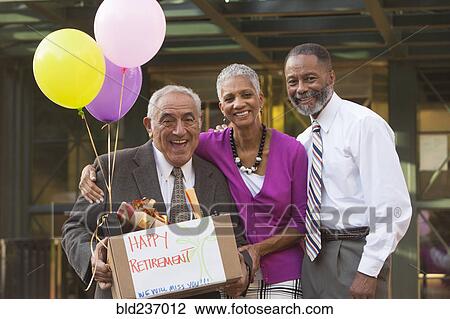 Stock Image - Co-workers posing with retiring man carrying belongings. Fotosearch