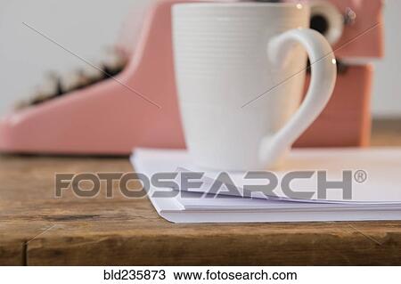 Stock Image - Coffee cup on pile of paper near pink typewriter. Fotosearch