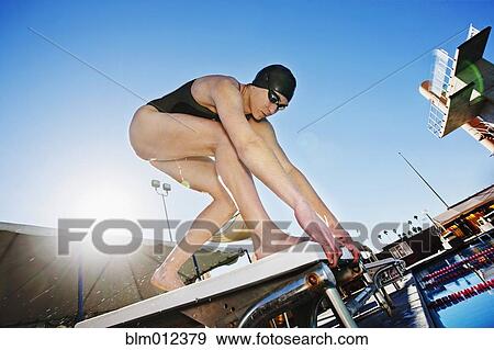 Stock Photo - Competitive swimmer crouching on starting block. Fotosearch