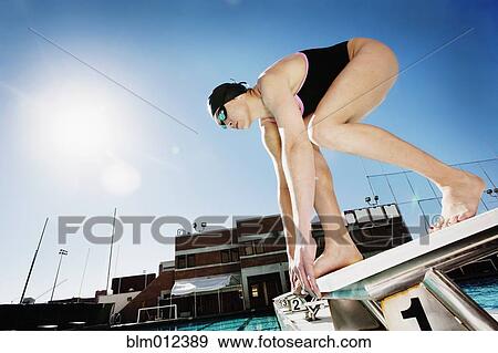 Stock Photo - Competitive swimmer crouching on starting block. Fotosearch