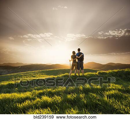 Stock Photo - Couple hugging on hill at sunset. Fotosearch