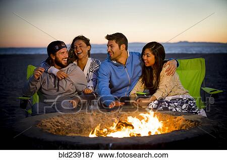 Stock Photo - Couple relaxing on beach at fire pit. Fotosearch