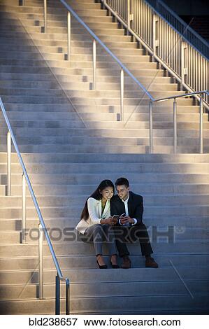 Couple sitting on staircase texting on cell phones View Large Photo Image Stock Photo - Couple sitting on staircase texting on cell phones. Fotosearch