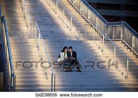 Couple sitting on staircase texting on cell phones View Large Photo Image Stock Photograph - Couple sitting on staircase texting on cell phones. Fotosearch