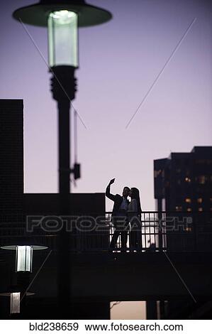 Couple standing on balcony posing for cell phone selfie at night View Large Photo Image Stock Photo - Couple standing on balcony posing for cell phone selfie at night. Fotosearch